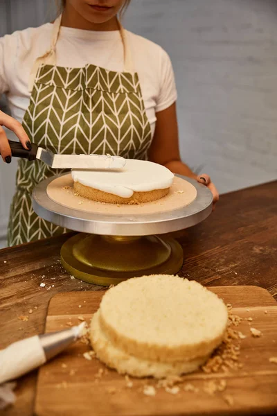 Vista cortada de confeiteiro usando espátula para creme doce na camada de bolo — Fotografia de Stock