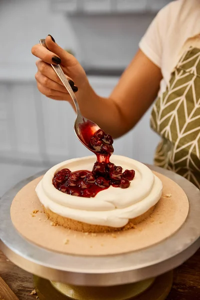 Cropped view of confectioner putting berry jam on cake layer with cream — Stock Photo