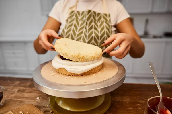 Vista cortada de confeiteiro colocando camada no bolo de esponja com creme — Fotografia de Stock