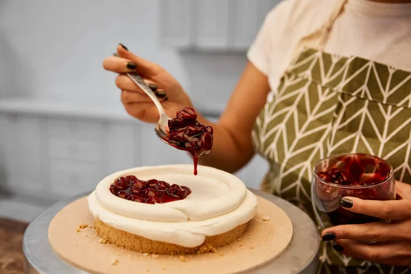 Abgeschnittene Ansicht des Konditors, der leckere Beerenmarmelade auf Kuchen hinzufügt — Stockfoto