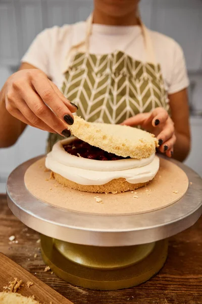 Cropped view of confectioner putting layer on biscuit with cream on stand — Stock Photo