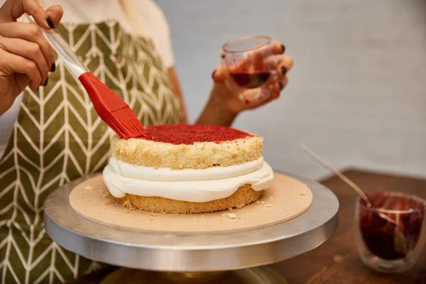 Cropped view of confectioner working with pastry brush and jam on biscuit — Stock Photo