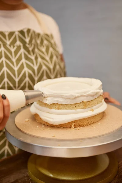 Vista recortada del pastelero con bolsa de pastelería añadiendo crema sobre galleta en soporte aislado en gris - foto de stock