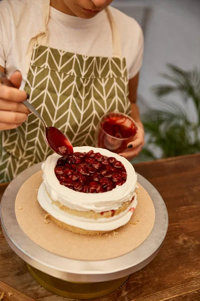 Gehackte Ansicht des Konditors, der leckere Beerenmarmelade auf Kuchenschicht hinzufügt — Stockfoto