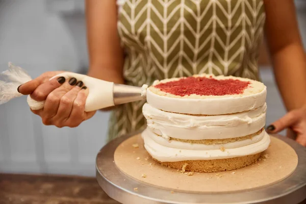 Vista ritagliata del pasticciere con sacchetto di pasticceria con crema durante la preparazione della torta — Foto stock