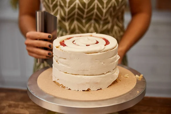 Cropped view of confectioner working with scraper and cake — Stock Photo