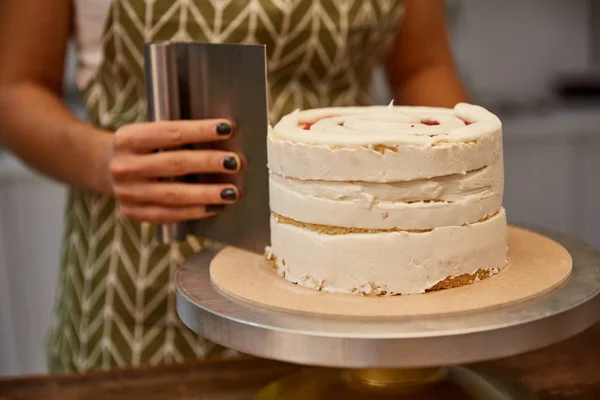Vista cortada de confeiteiro usando raspador para alinhar creme no bolo — Fotografia de Stock
