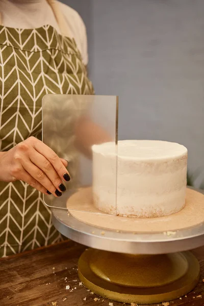 Vue recadrée du confiseur à l'aide d'un grattoir transparent sur la crème à gâteau — Photo de stock