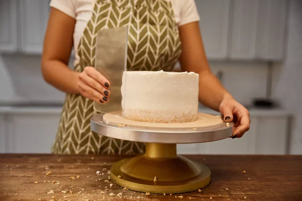 Vista recortada de la crema alineadora confitera femenina con raspador en la torta de esponja - foto de stock