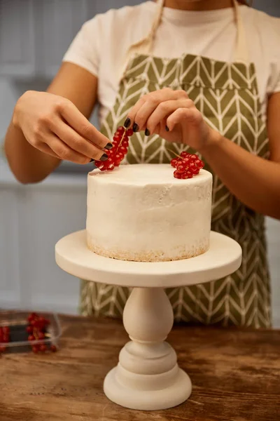 Cropped view of confectioner adding redcurrant on cake — Stock Photo