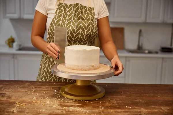 Cropped view of woman aligning cream on biscuit with scraper on stand — Stock Photo