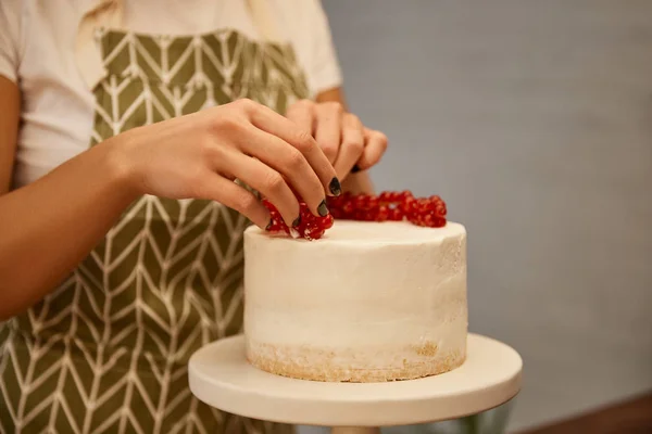Vista ritagliata di pasticciere che aggiunge il ribes rosso su torta saporita con crema — Foto stock