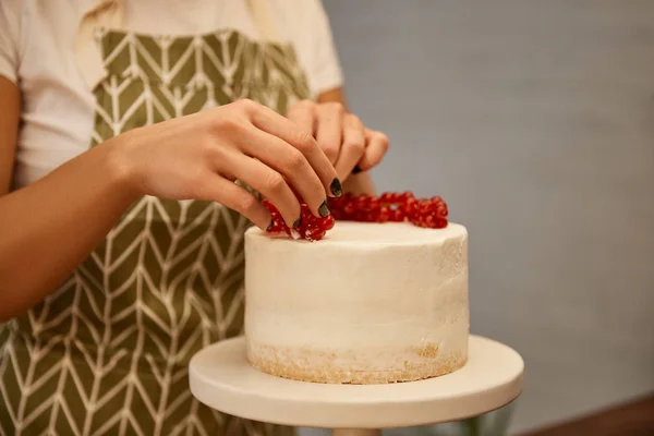 Cropped view of confectioner adding redcurrant on tasty cake with cream — Stock Photo