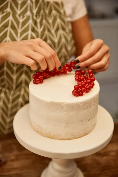 Cropped view of confectioner putting juicy redcurrant on cake with cream — Stock Photo