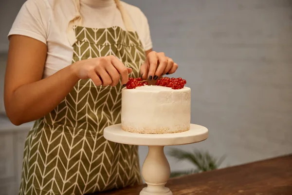 Cropped view of confectioner decorating sponge cake with fresh redcurrant — Stock Photo