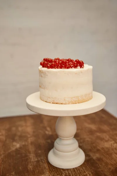 Gâteau à l'éponge sucrée avec crème et groseille juteuse sur support de gâteau sur table en bois — Photo de stock