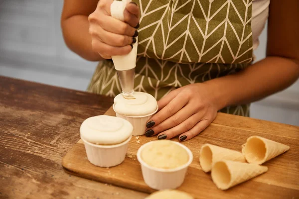 Vista ritagliata del pasticciere aggiungendo gustosa crema sui cupcake al forno — Foto stock