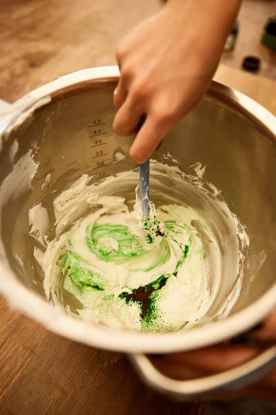 Vista cortada de creme de mistura de confeiteiro com corante de alimentos verdes na tigela — Fotografia de Stock