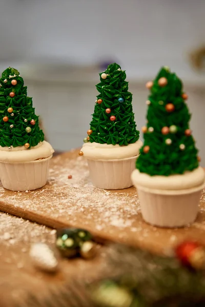 Selective focus of Christmas tree cupcakes with green cream and christmas balls with spruce branch on table — Stock Photo