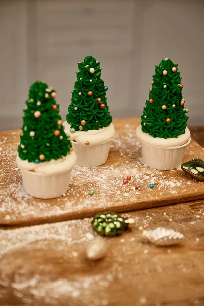 Tasty Christmas tree cupcakes with green cream and decorations on cutting board with christmas balls — Stock Photo