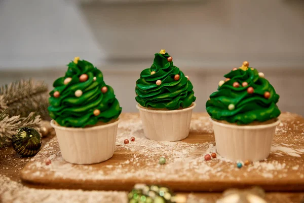 Pastelitos decorados con crema verde y bolas de Navidad con rama de abeto en la mesa - foto de stock