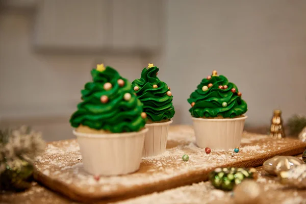 Selektiver Fokus von süßen Cupcakes mit Weihnachtskugeln und Fichtenzweigen auf Schneidebrett — Stockfoto