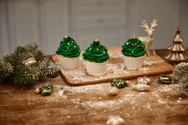 Cupcakes com polvilhas de açúcar e bolas de Natal com ramos de abeto na mesa — Fotografia de Stock