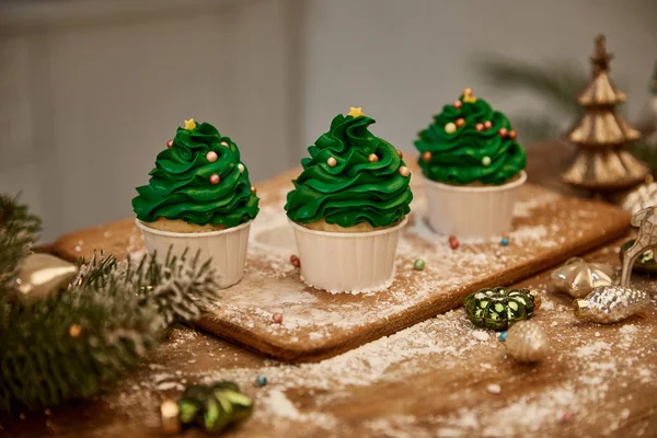 Вкусные кексы с рождественскими шарами и еловой веткой на столе — стоковое фото