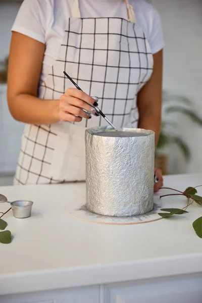 Vista recortada del pastel decorativo confitero con cepillo junto a hojas de plantas en la mesa - foto de stock