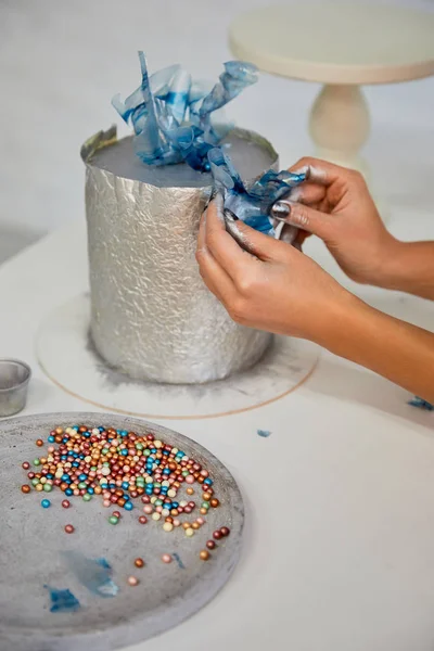 Vista ritagliata del pasticciere che decora la torta con zuccherini sul tavolo — Foto stock
