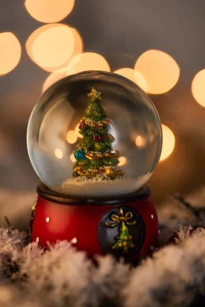 Декоративный снежок с рождественской ёлкой, стоящей в снегу с золотыми огнями боке — стоковое фото