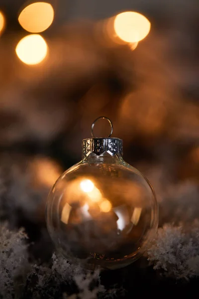 Transparent christmas ball on spruce branches in snow with blurred yellow lights in dark — Stock Photo