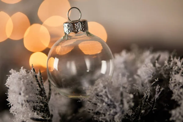 Decorative transparent christmas ball on spruce branches in snow with blurred yellow lights — Stock Photo