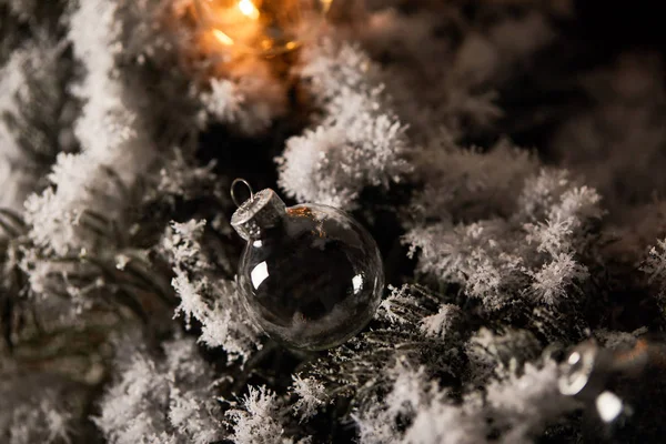 Transparent christmas balls and yellow lights on spruce branches in snow — Stock Photo