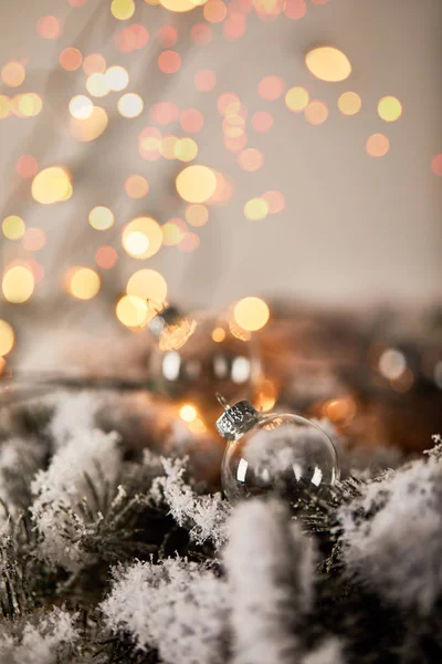 Transparent christmas balls on spruce branches in snow with blurred yellow lights — Stock Photo