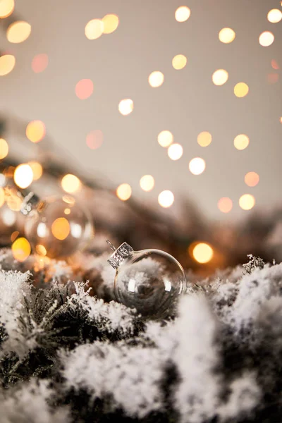 Boules de Noël transparentes sur les branches d'épinette dans la neige avec des lumières jaunes floues — Photo de stock