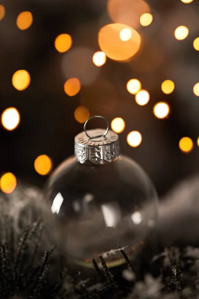 Крупним планом прозорий різдвяний м'яч на ялинових гілках у снігу з жовтими вогнями боке — стокове фото