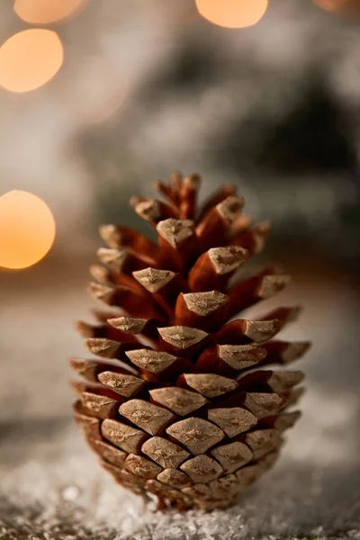 Gros plan de cône de pin sur la neige avec des lumières de Noël bokeh — Photo de stock