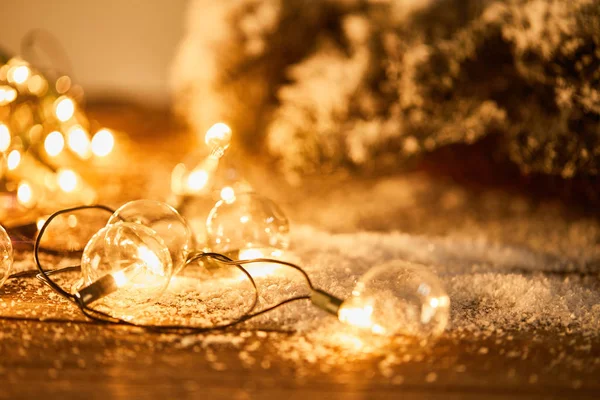 Guirlande de Noël avec ampoules transparentes sur la surface en bois avec branches d'épinette dans la neige — Photo de stock