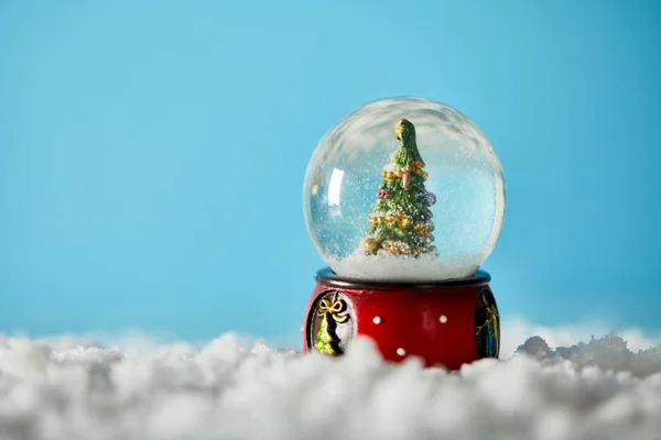 Árbol de navidad en bola de nieve de pie sobre azul con nieve - foto de stock