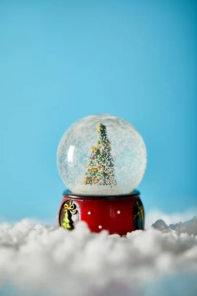 Árbol de navidad en bola de nieve de pie sobre azul con nieve - foto de stock