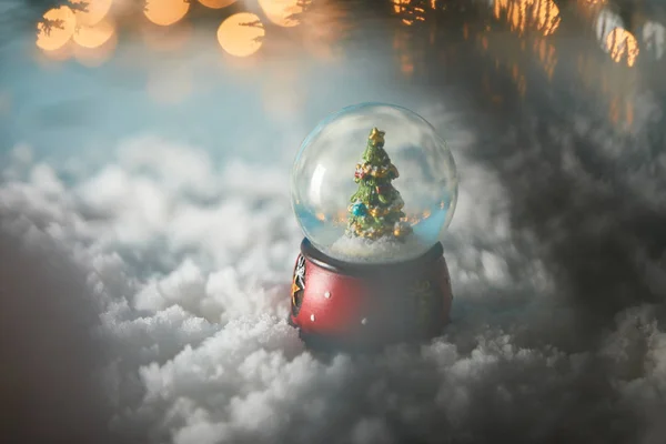 Selective focus of decorative snowball with christmas tree standing on blue in snow with lights bokeh — Stock Photo