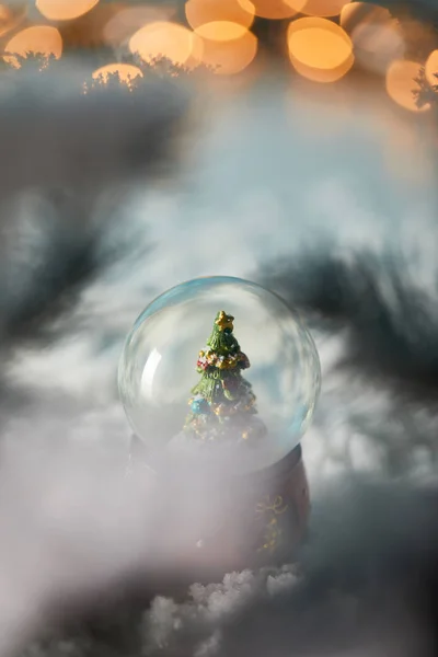 Selective focus of snowball with christmas tree standing on blue in snow with spruce branches and lights bokeh — Stock Photo