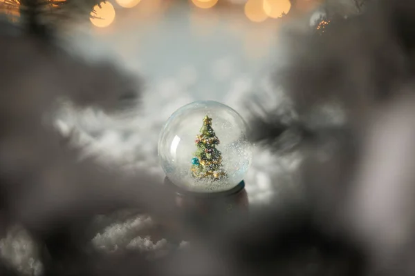 Selective focus of little snowball with christmas tree standing in snow with spruce branches and lights bokeh — Stock Photo