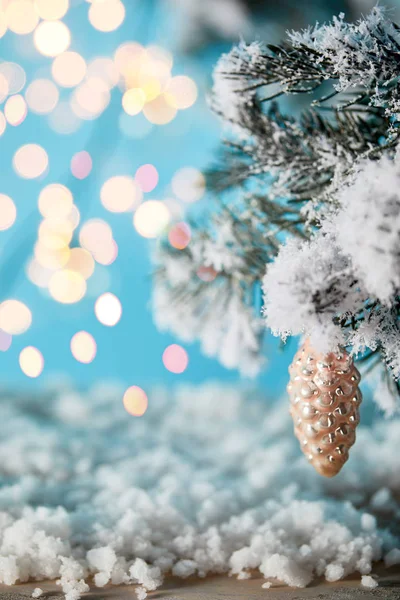Spruce branches in snow with christmas ball pine cone and blurred lights on blue — Stock Photo