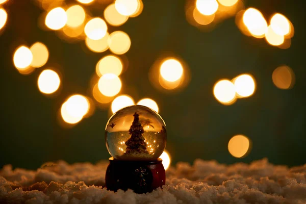 Pequeña bola de nieve con árbol de Navidad de pie en la nieve con luces borrosas en la noche - foto de stock