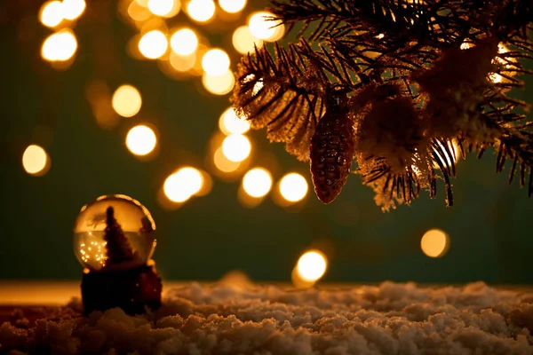 Little snowball with christmas tree standing in snow with spruce branches, christmas ball and blurred lights at night — Stock Photo
