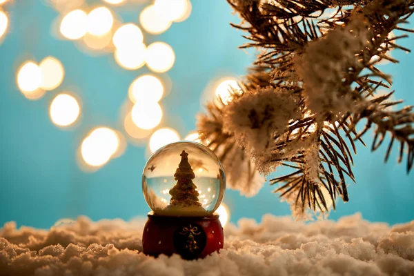 Decorative christmas tree in snowball standing on blue with spruce branches in snow and blurred lights — Stock Photo
