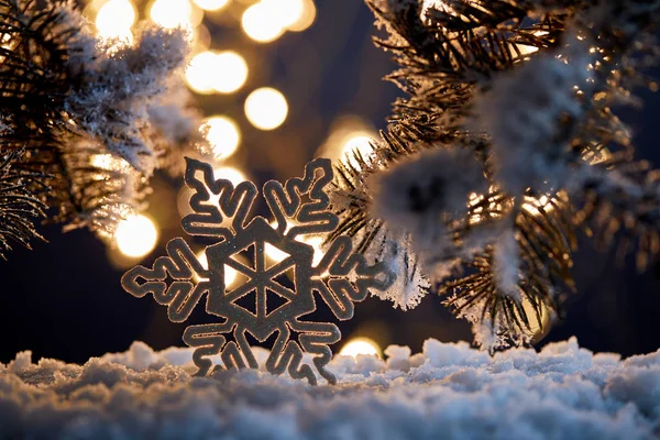 Close up of decorative snowflake with spruce branches in snow with blurred christmas lights — Stock Photo