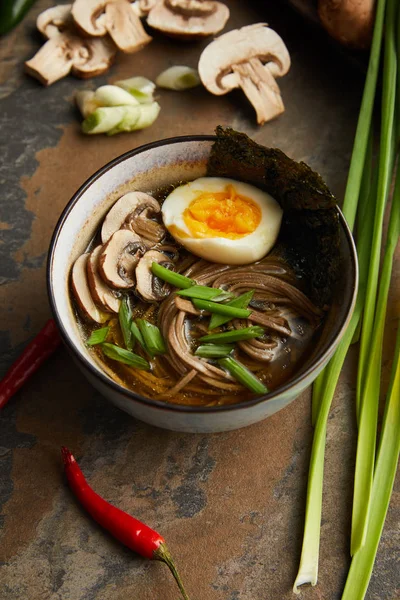 Ramen piccante tradizionale in ciotola vicino a verdure su superficie di pietra — Foto stock